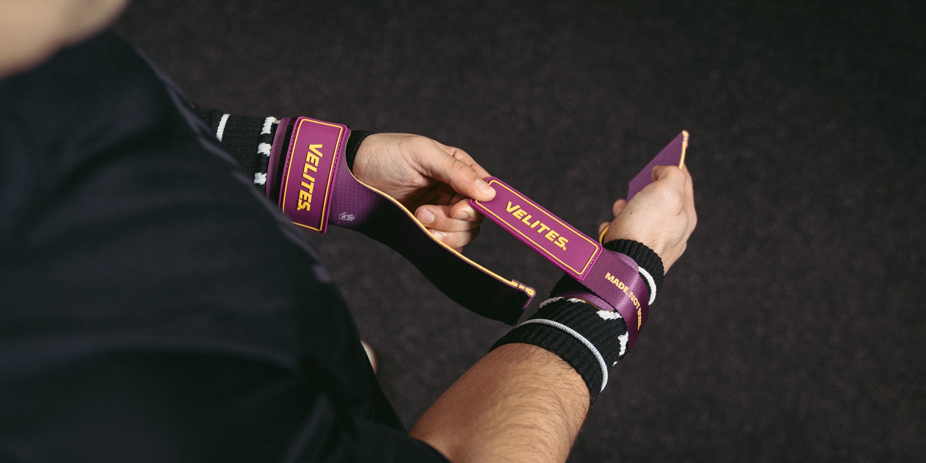 Athlete tightening purple Velites hand grips with black wrist wraps before a CrossFit workout, showing the Velites logo